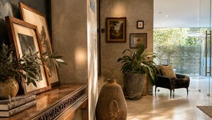 Un interior moderno con un banco de madera, cuadros enmarcados, plantas en macetas, un jarrón grande y un sofá.