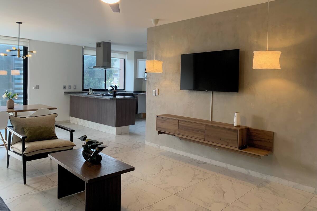 Una sala de estar moderna con un televisor montado en la pared, un comedor con isla de cocina y un ventilador de techo.