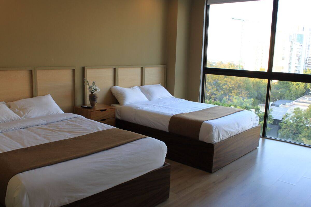 Habitación de hotel con dos camas, una mesita de noche y un ventanal con vistas a la ciudad.