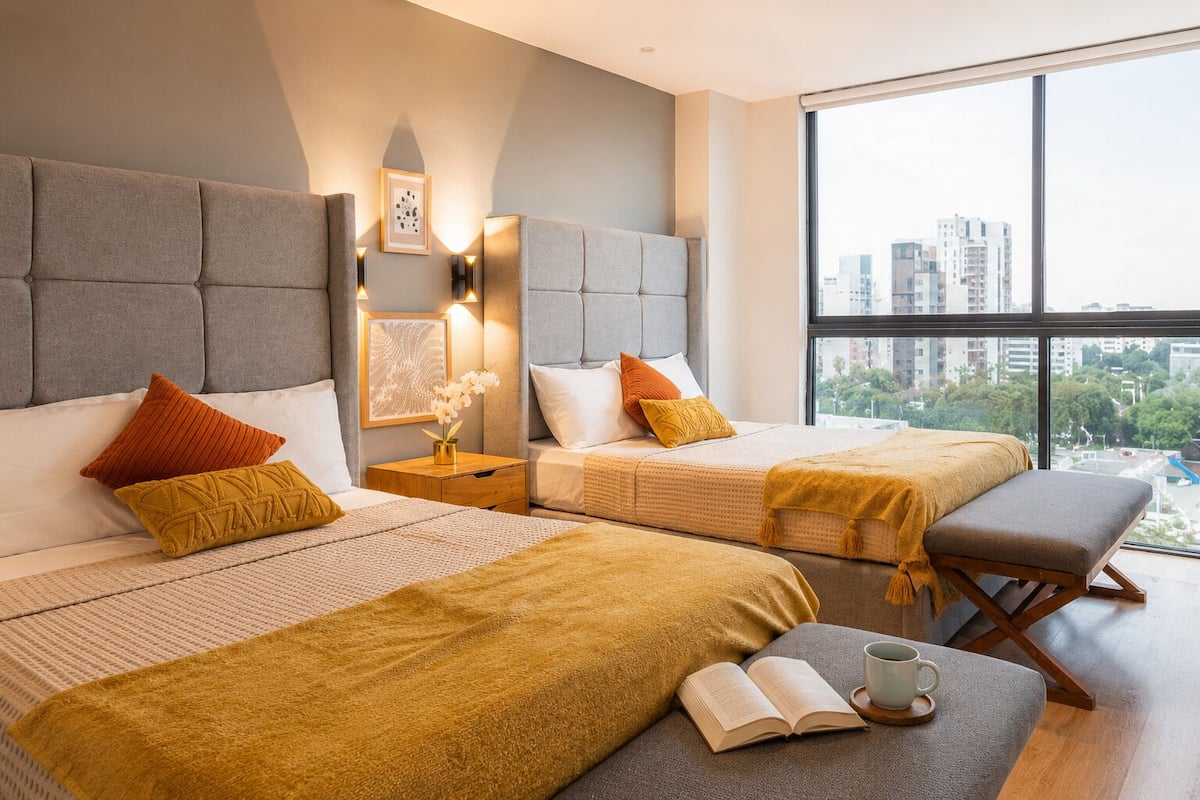 Una habitación de hotel moderna con dos camas, un ventanal grande y vistas a la ciudad.