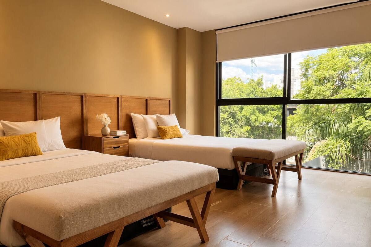 Habitación de hotel con dos camas, cabecero de madera, mesita de noche y un ventanal con vistas a zonas verdes.