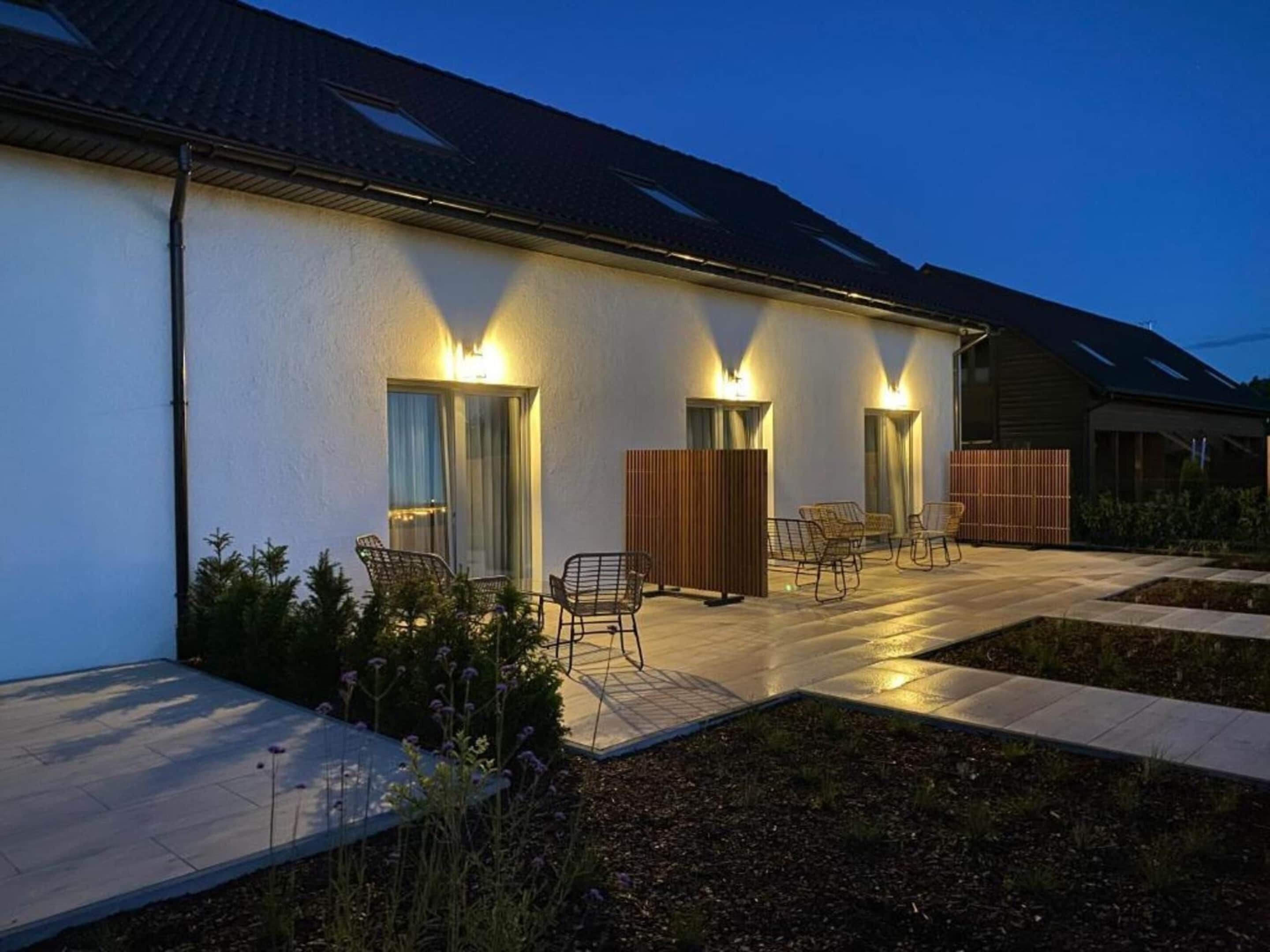 A modern house with a patio, outdoor seating, and a well-lit entrance.