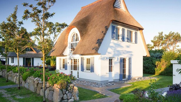 Une maison à deux étages, avec un toit de chaume, des murs extérieurs blancs et des fondations en pierre.
