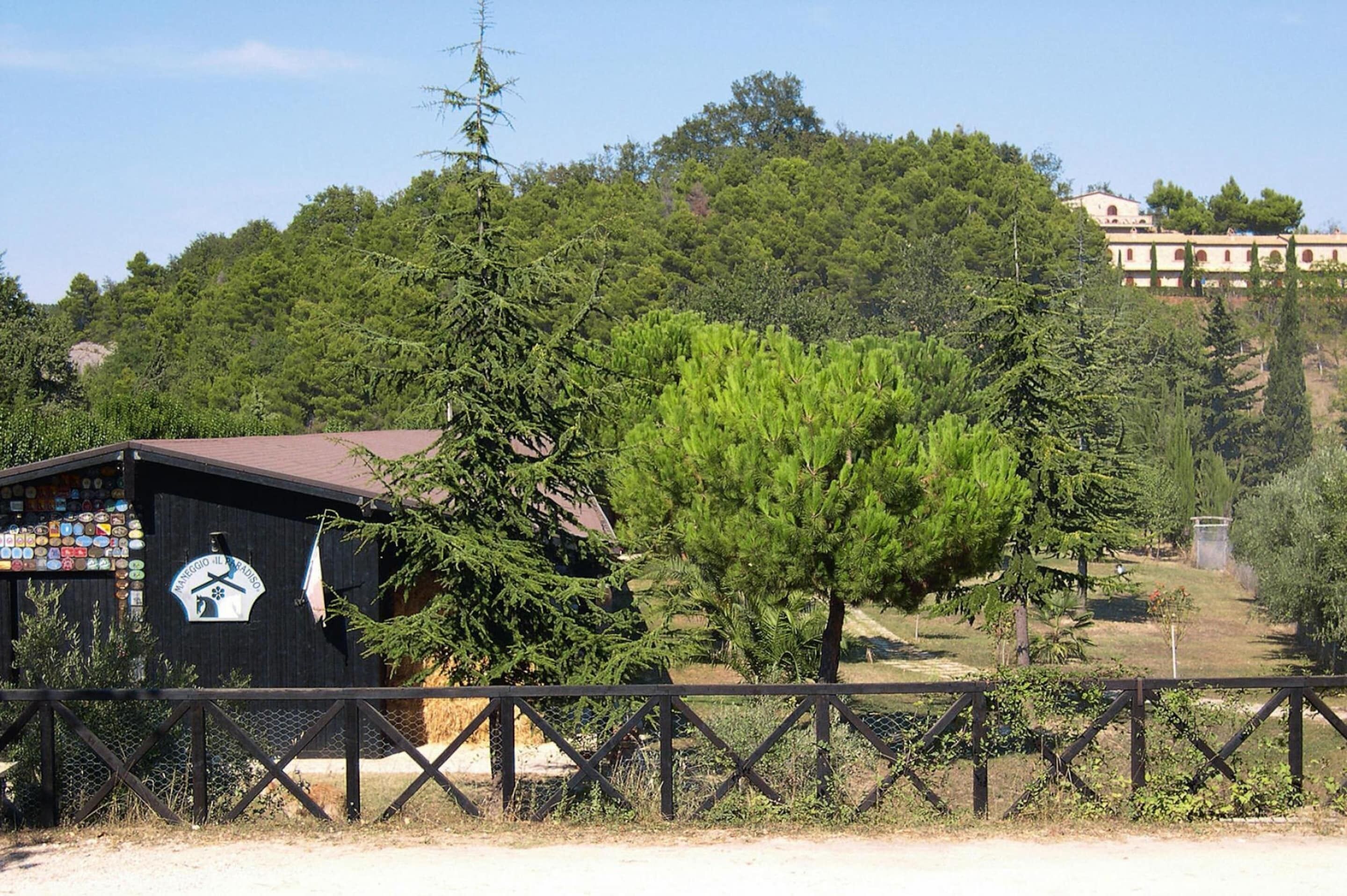 A rustic wooden building with a sign, surrounded by lush greenery and a fence.