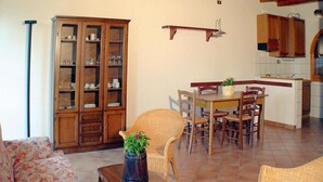 Amplia sala de estar con mesa y sillas de comedor, un sofá de mimbre y un aparador con puertas de vidrio.