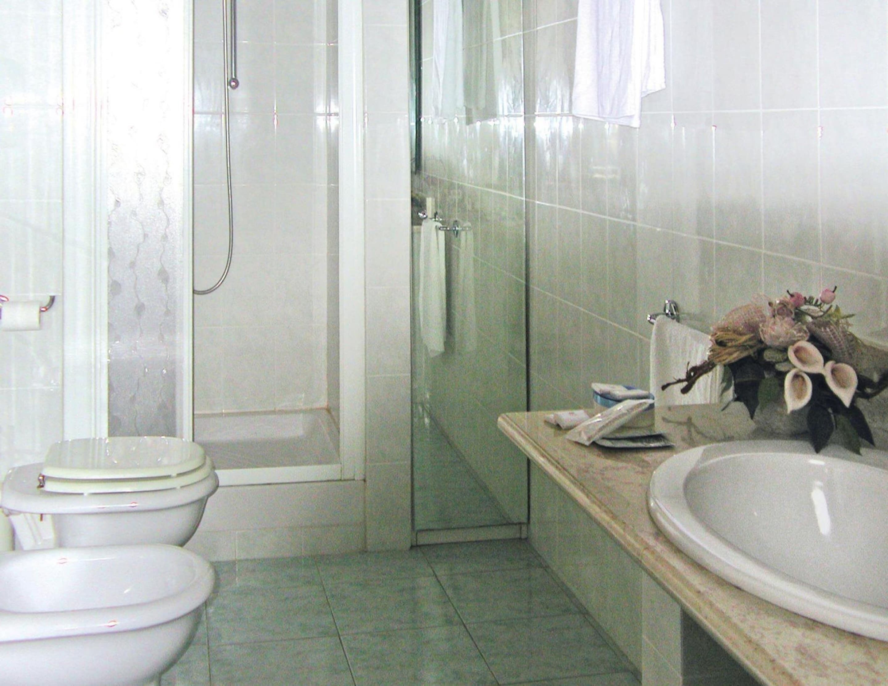 A bathroom with two toilets, a shower, and a sink with a vase of flowers.
