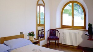 Un dormitorio con cama, una silla, un ventanal y un radiador.