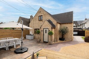 A stone house with a tiled roof, a wooden fence, and a patio with a table and chairs.
