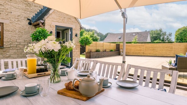 A breakfast setup with a table, chairs, and a large umbrella. - Incredible dog friendly holiday home in the Cotswolds with a hot tub - Puddleduck House (Bourton-on-the-Water)