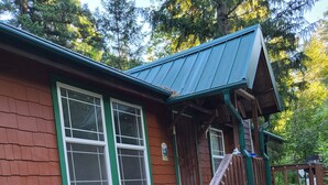 A wooden cabin with a green roof, a front porch, and a small deck. - Private enchanting cabin on the river  (McKenzie Bridge)