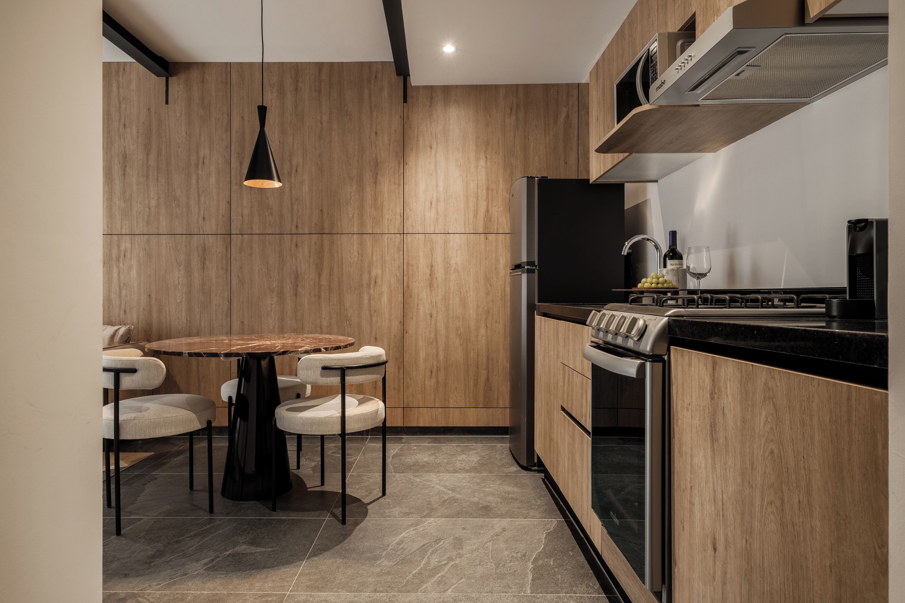 A modern kitchen with wooden cabinets, a black refrigerator, a gas stove, and a round dining table with chairs.
