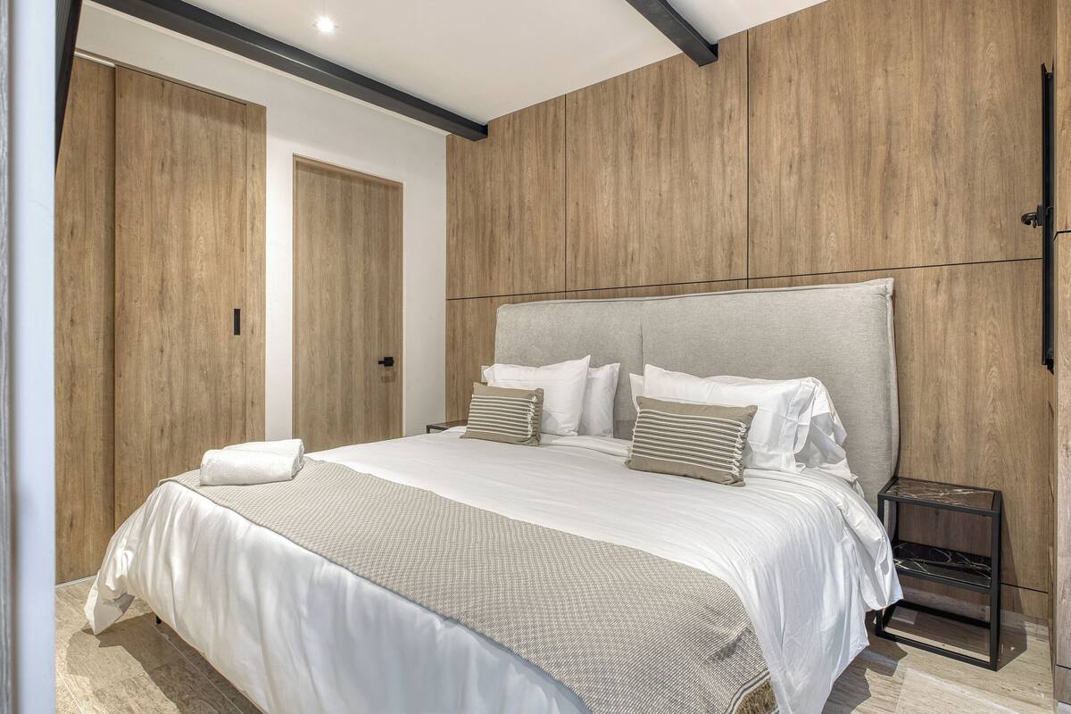 A modern bedroom with a large bed, wooden panel walls, and a minimalist nightstand.