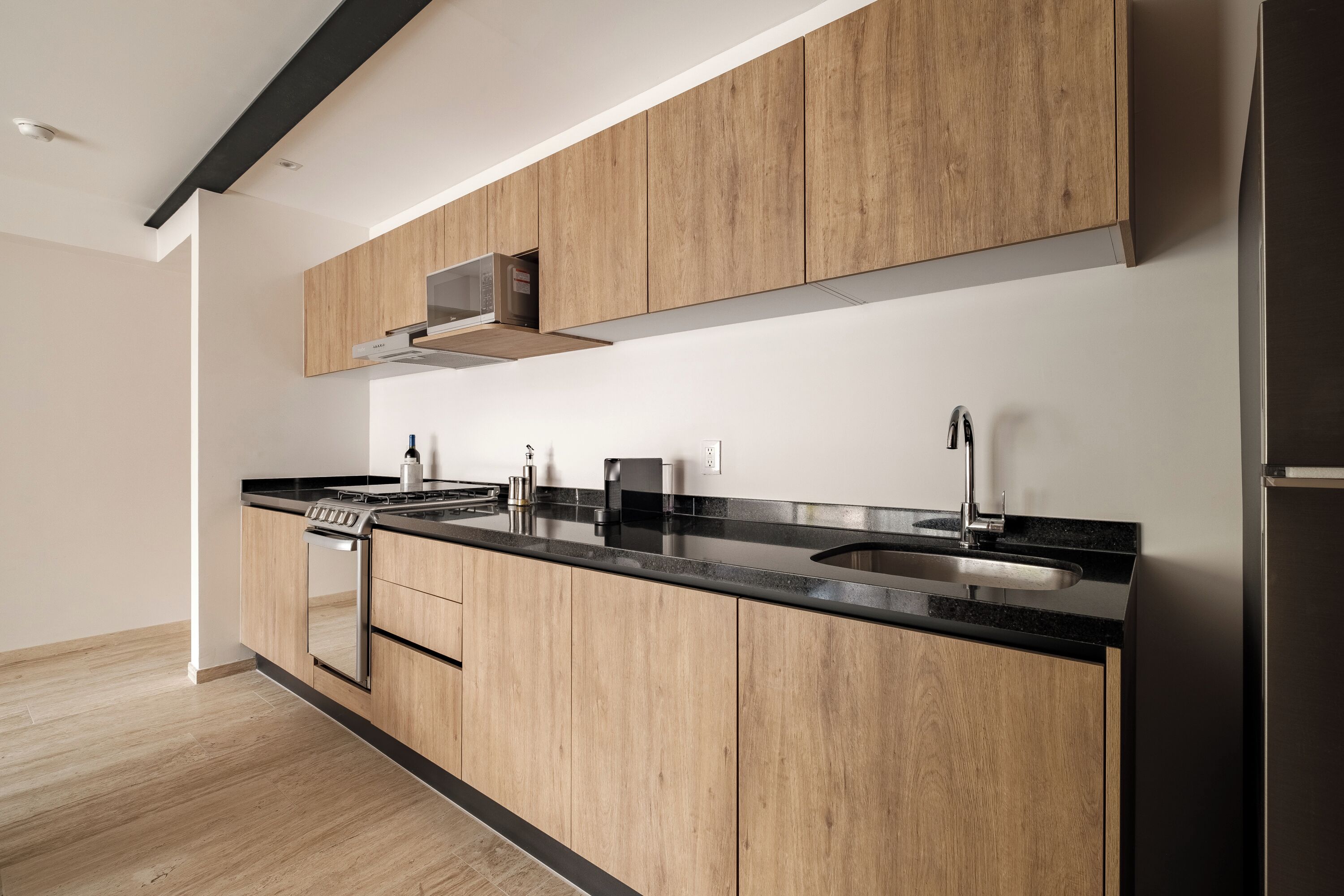 Une cuisine moderne avec des meubles en bois, un plan de travail noir, des appareils électroménagers en acier inoxydable et un micro-ondes encastré.