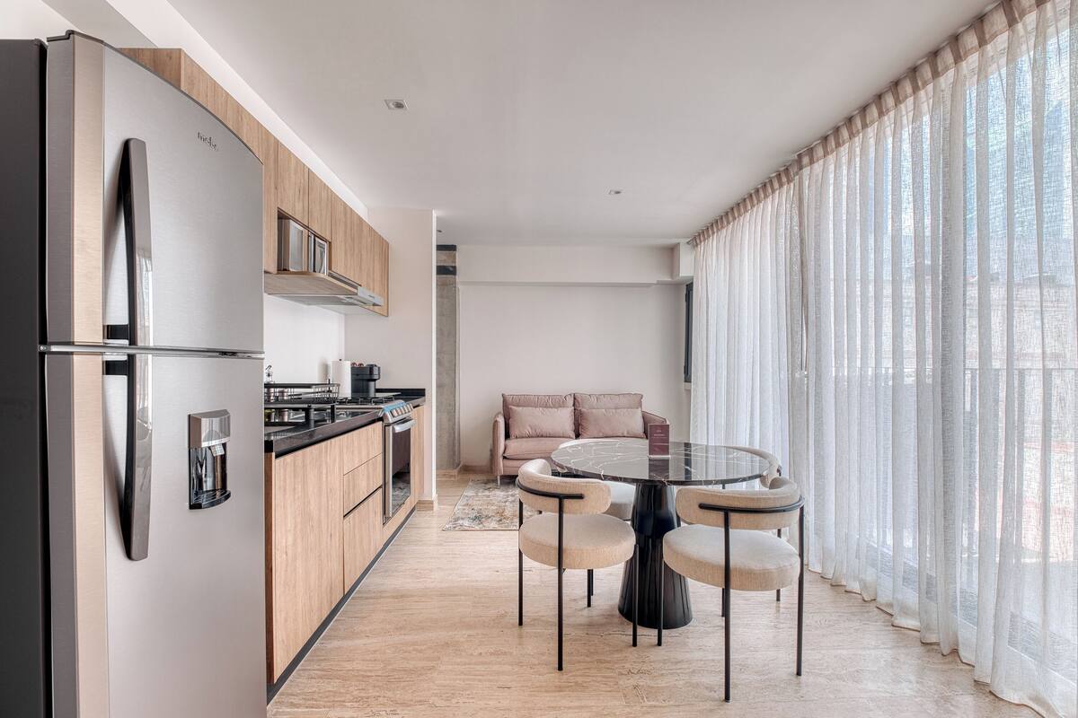 A modern kitchen with a refrigerator, wooden cabinets, and a dining area with a round table and chairs.