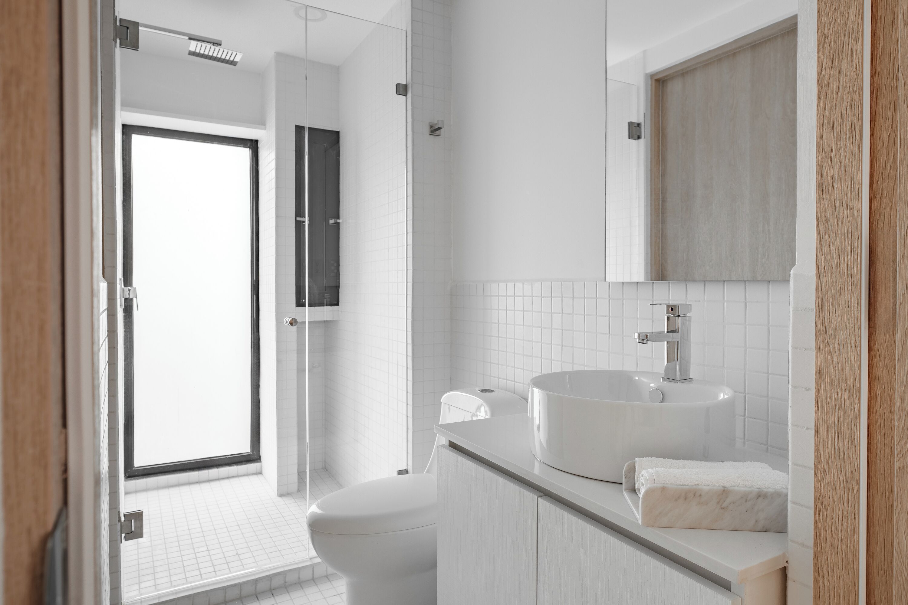 A modern bathroom with a white toilet, a sink with a marble countertop, and a wooden vanity.