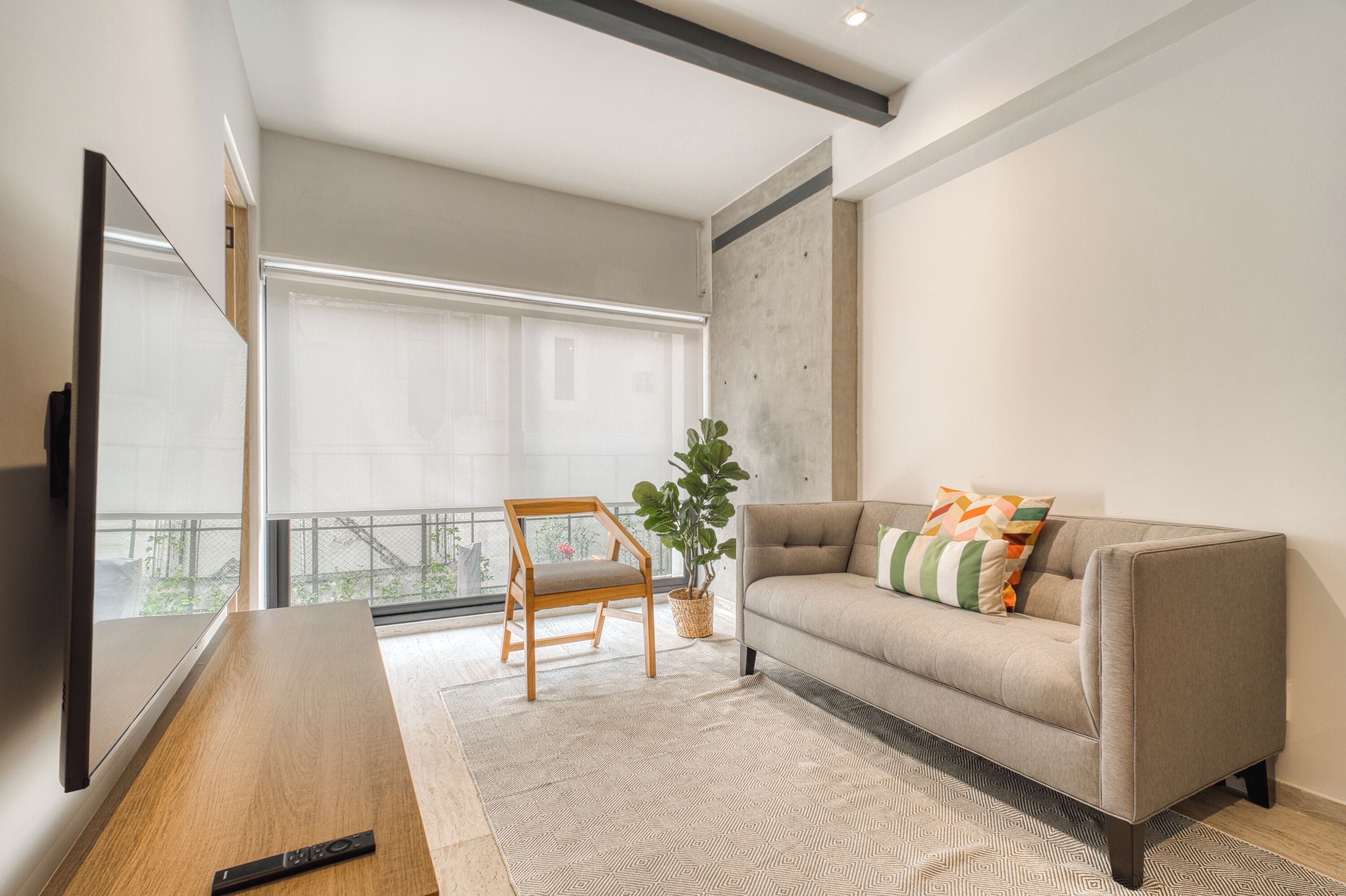 A modern living room with a sofa, a wooden chair, a TV, and a large window with a view.