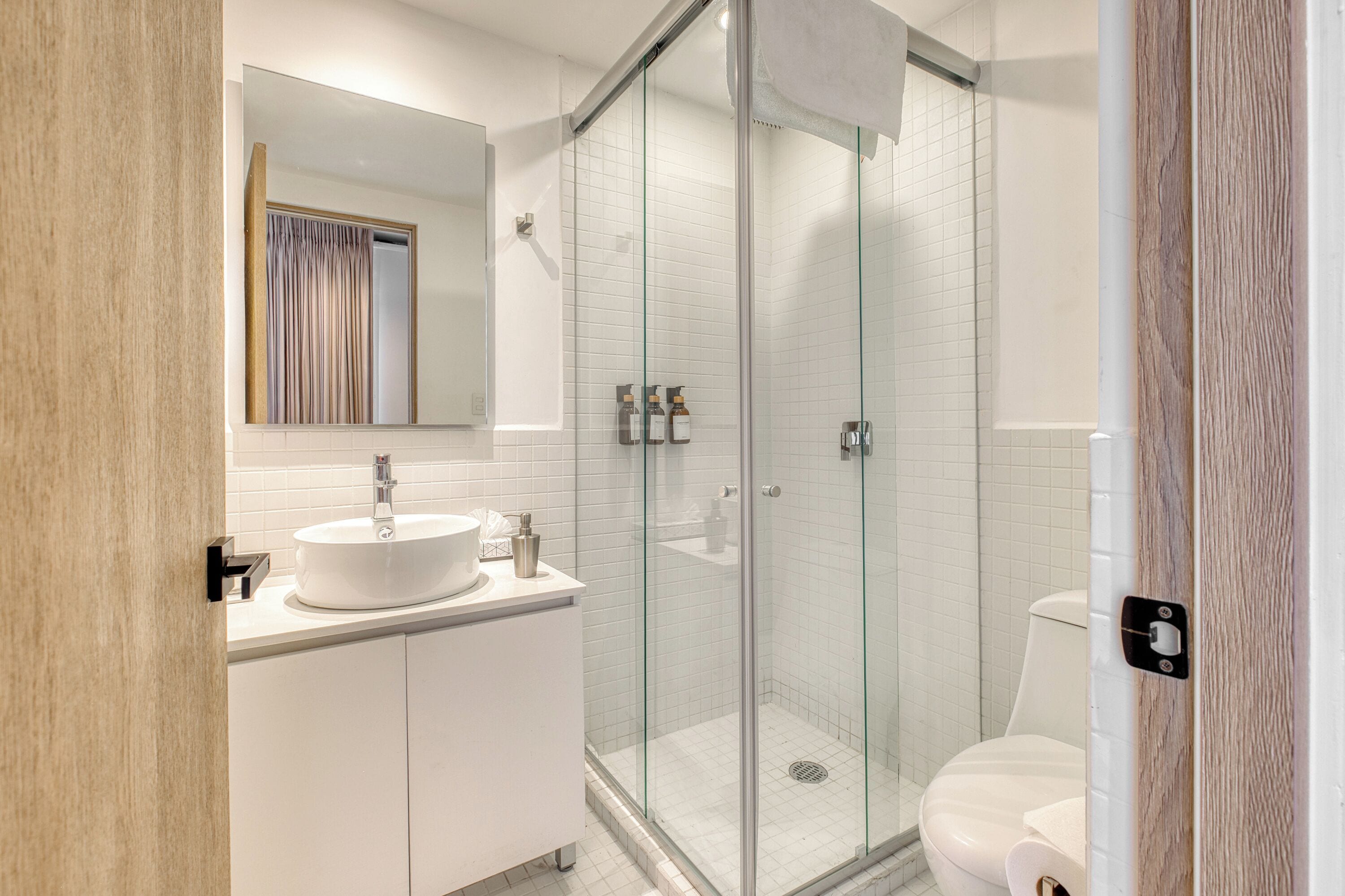 Un baño moderno con cabina de ducha de vidrio, lavamanos blanco y retrete.