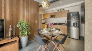 Eine moderne Küche mit Essbereich, mit einer Holzvertäfelung, Edelstahlgeräten und einem Glastisch mit schwarzen Stühlen.