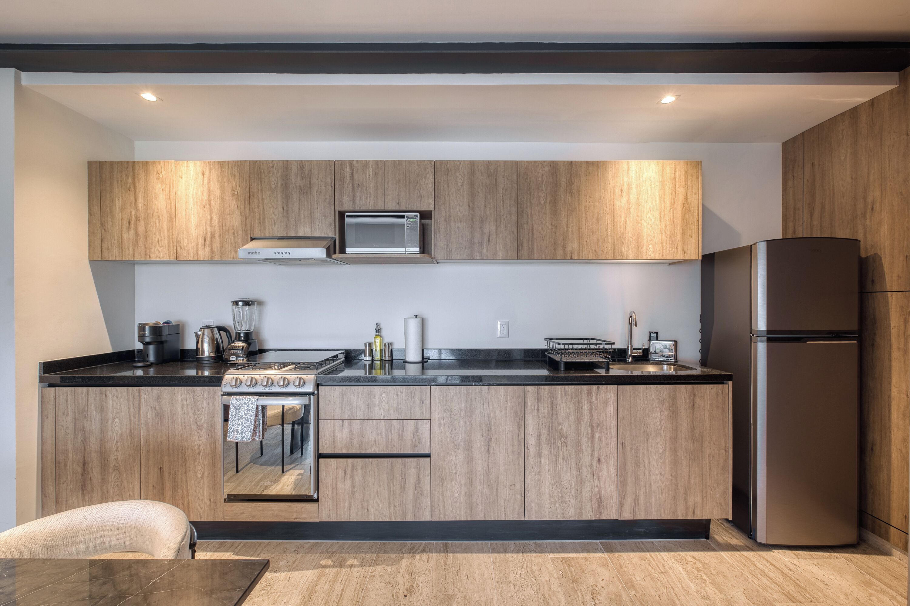 Une cuisine moderne avec des meubles en bois, un réfrigérateur en acier inoxydable, un four encastré et un four à micro-ondes.