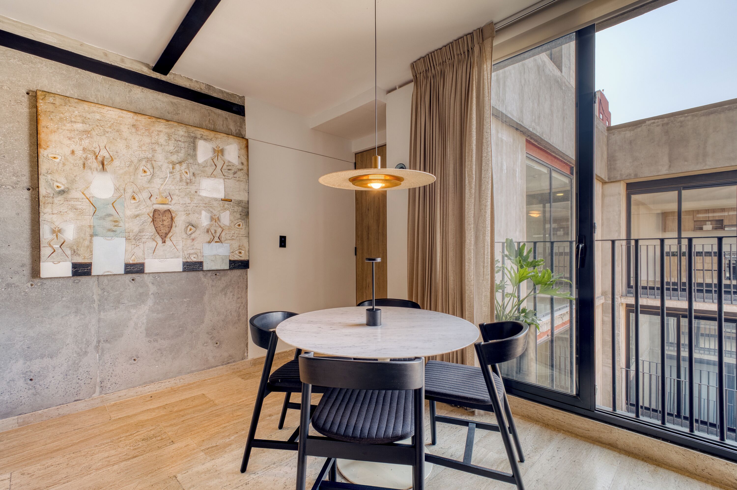 Et moderne spiseområde med et rundt bord, sorte stole, en hængende lampe og et stort abstrakt billede på væggen.