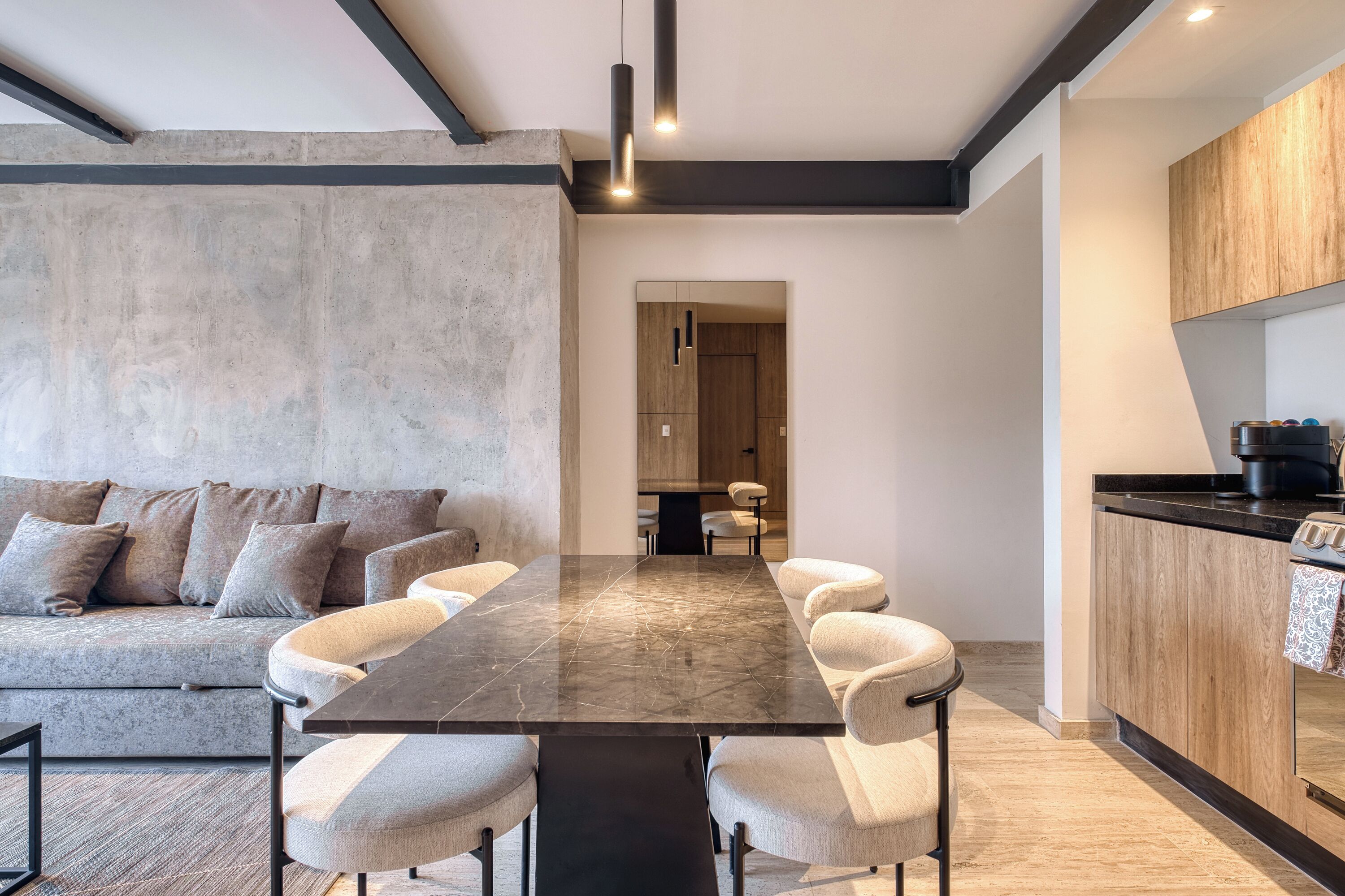 A modern kitchen with wooden cabinets, a black countertop, and a dining area with a marble table and upholstered chairs.