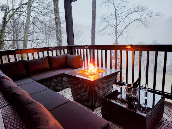 A deck with a fire pit, seating area, and a table with glasses and a bottle.