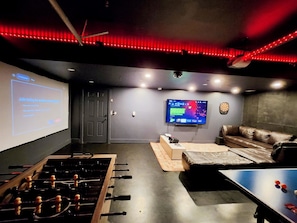 A room with a foosball table, a flat-screen TV, a sofa, and a dartboard.
