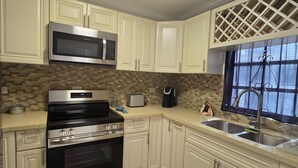 A modern kitchen with white cabinets, stainless steel appliances, a microwave, a stove, and a sink.