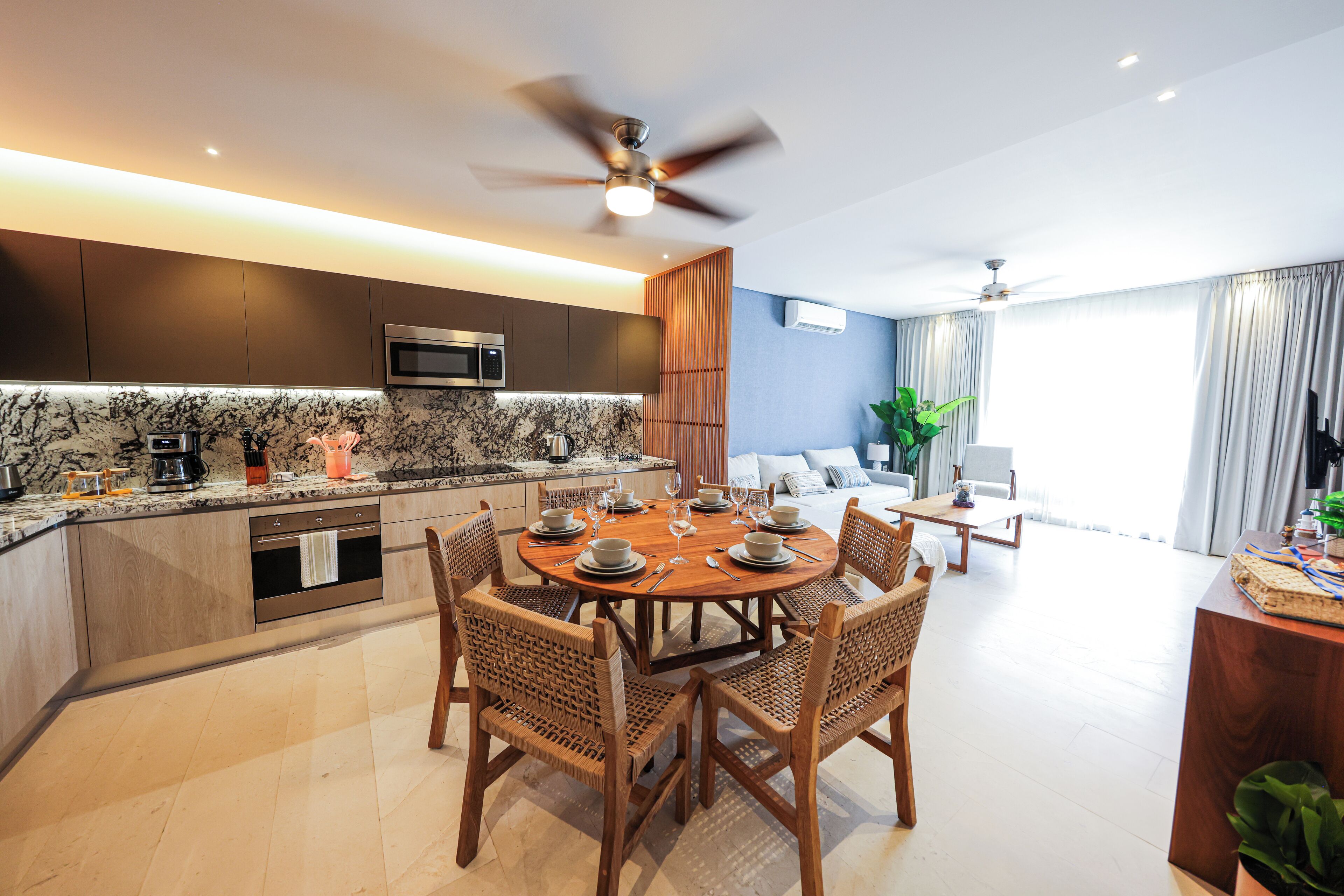 A modern kitchen with a dining area, wooden chairs, a round table, and a ceiling fan.
