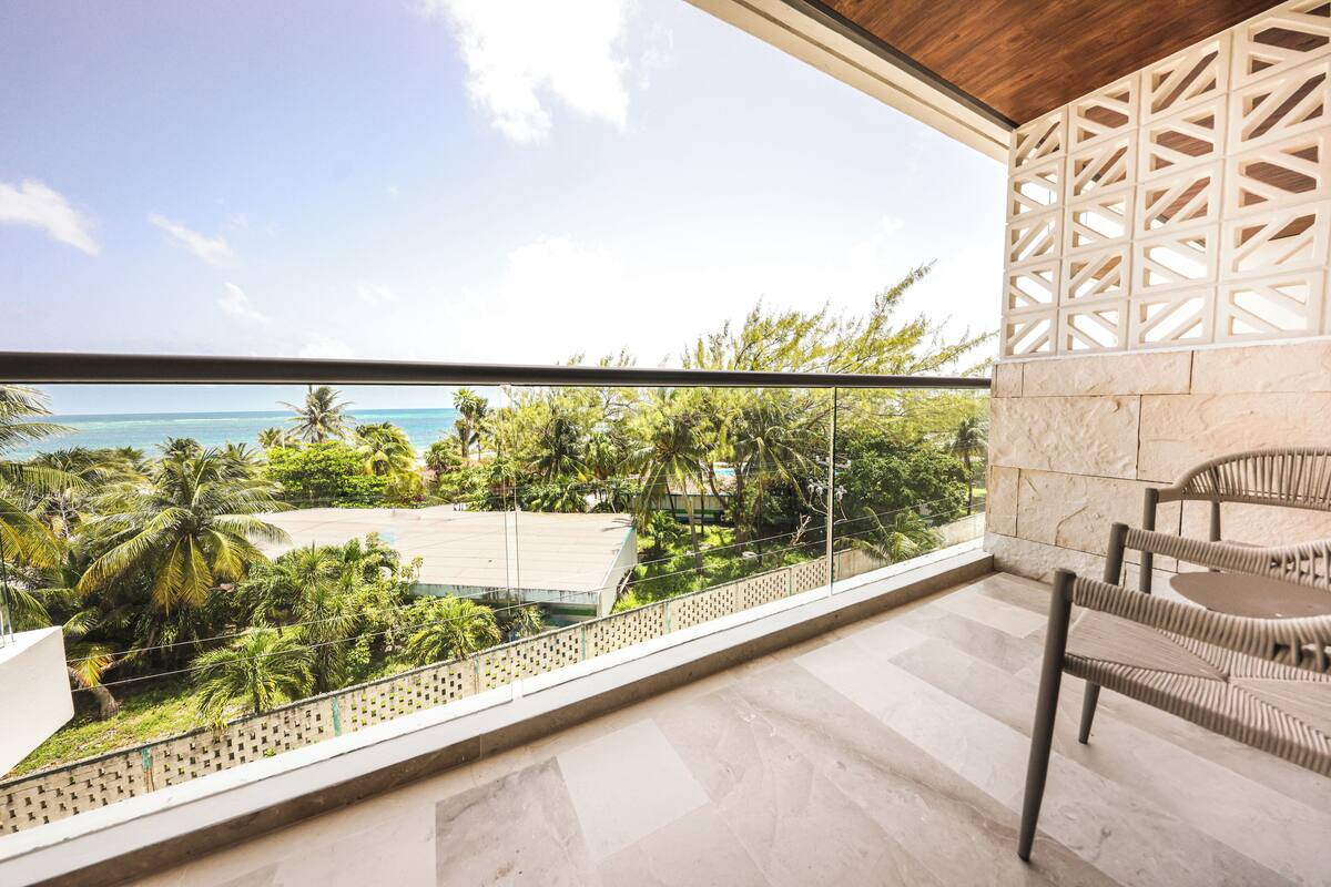 A balcony with a view of the ocean, palm trees, and a stone wall.