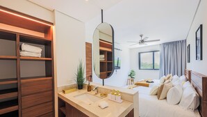 A modern hotel room with a large mirror, wooden wardrobe, dual sinks, and a bed with white linens.