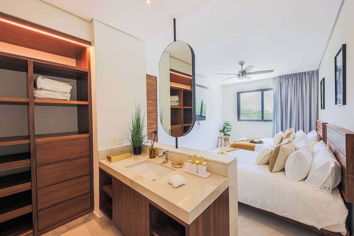 A modern hotel room with a large mirror, wooden wardrobe, dual sinks, and a bed with white linens.