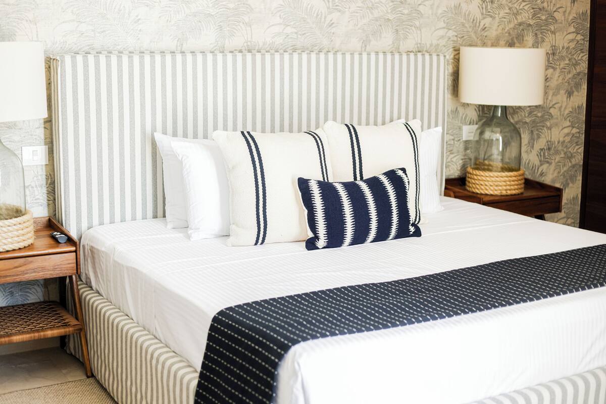 A neatly made bed with striped bedding, a bedside lamp, and a small wooden nightstand with a lamp and a decorative item.