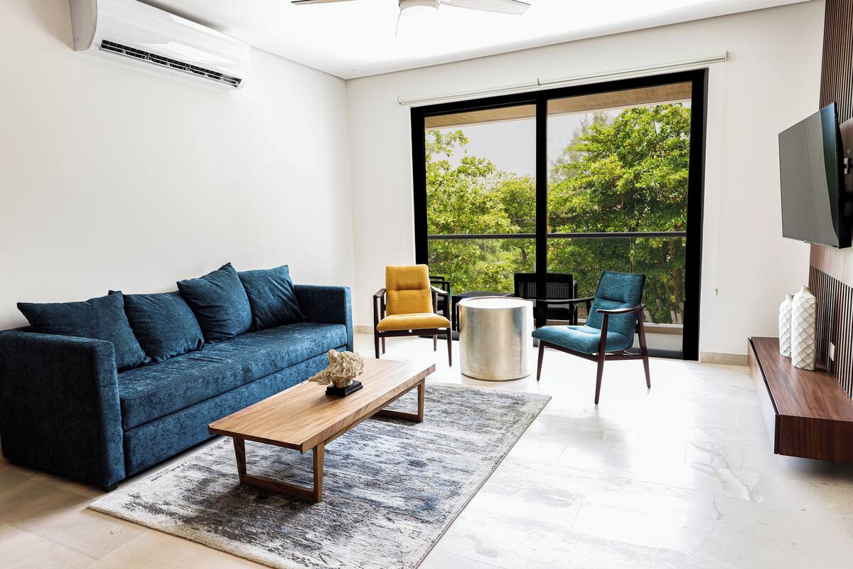 A modern living room with a blue sofa, a wooden coffee table, and two armchairs.