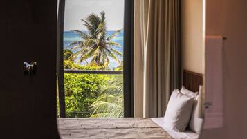 A bedroom with a bed, a ceiling fan, and a view of palm trees and the ocean through a large window.