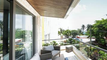 A balcony with wicker furniture, a glass table, and a view of the street and greenery.