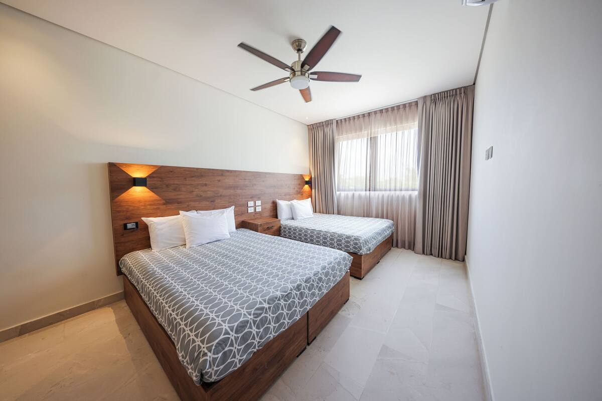 A hotel room with two beds, a ceiling fan, and a window with curtains.