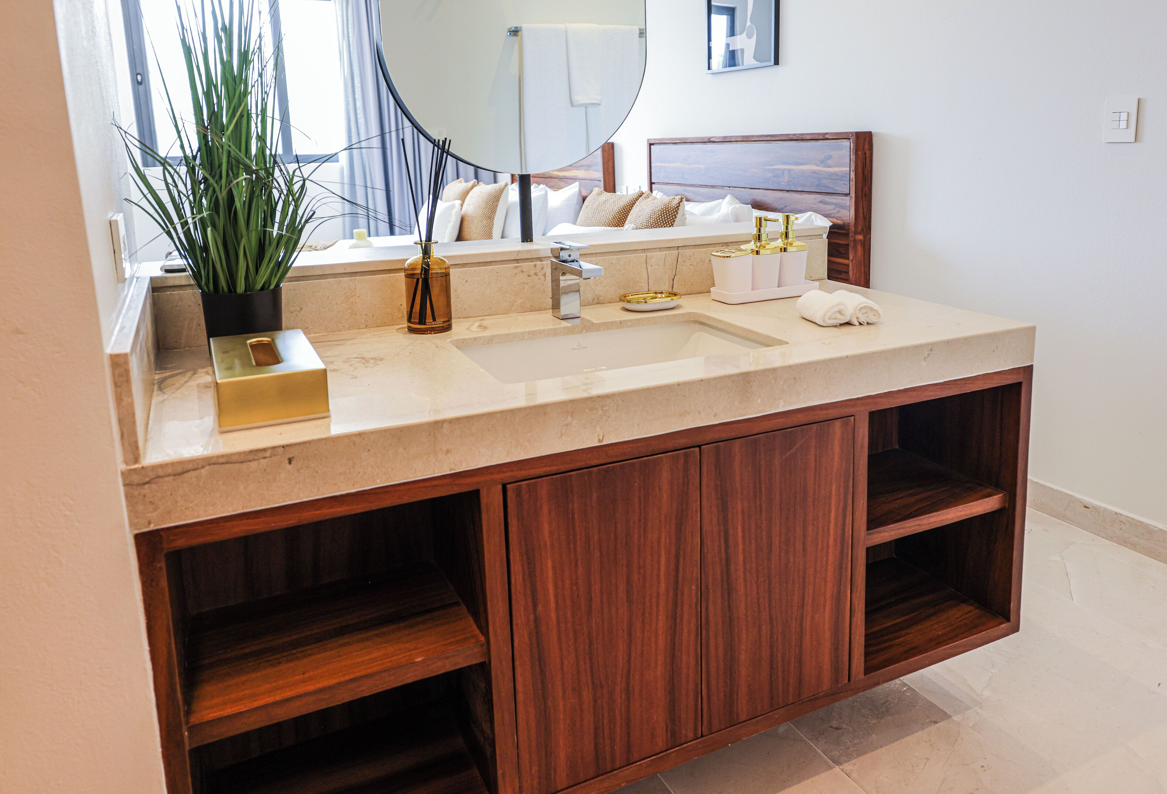 Une salle de bain avec un grand miroir, un lavabo avec un meuble-vasque, une plante en pot et un lit donnant sur une vue agréable.