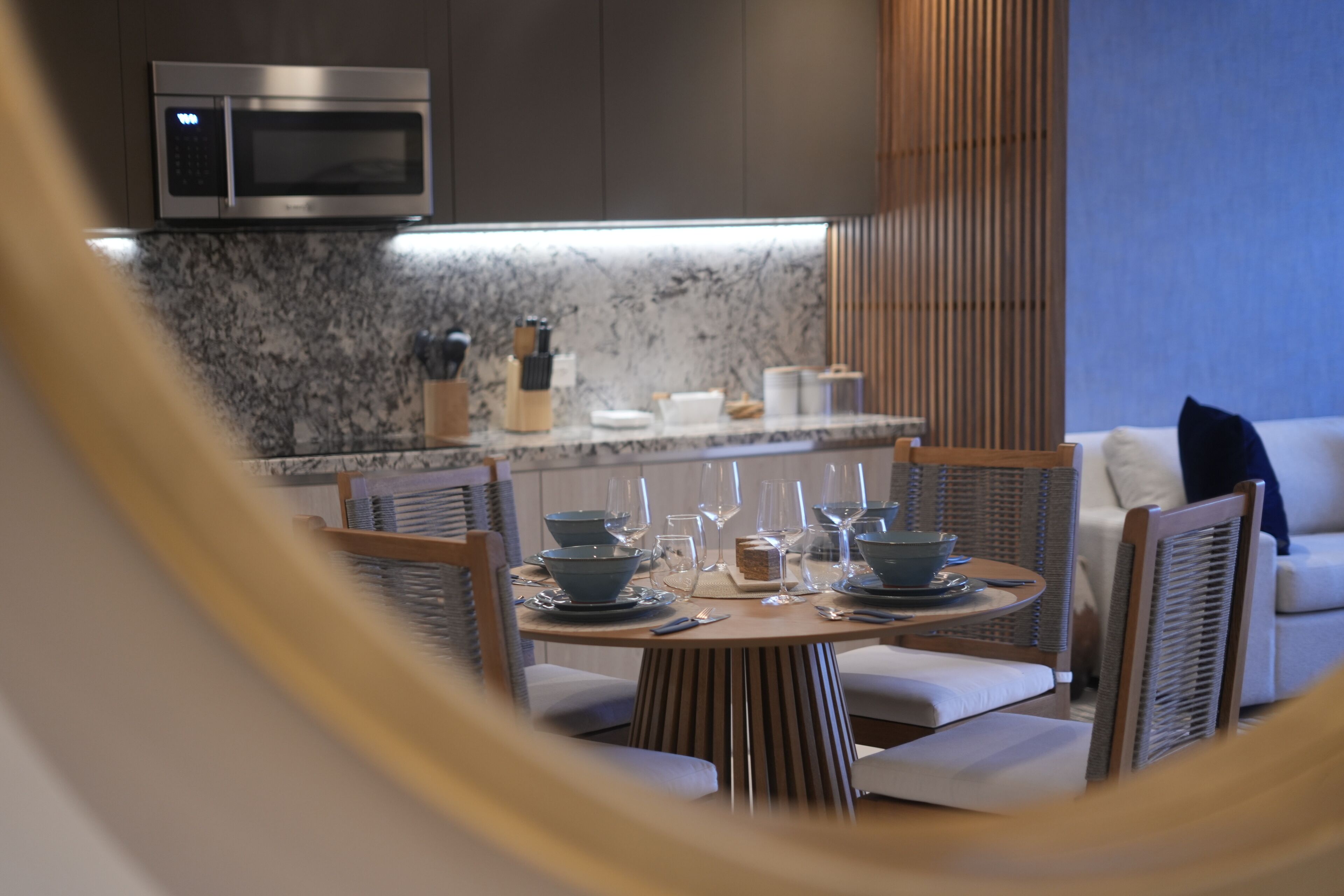 Un comedor moderno con una mesa redonda dispuesta para cuatro personas, con cuencos azules y copas de vino.