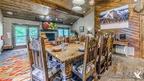 Un coin repas rustique avec des tables et des chaises en bois, une grande peinture au mur et une tête de cerf fixée au mur.