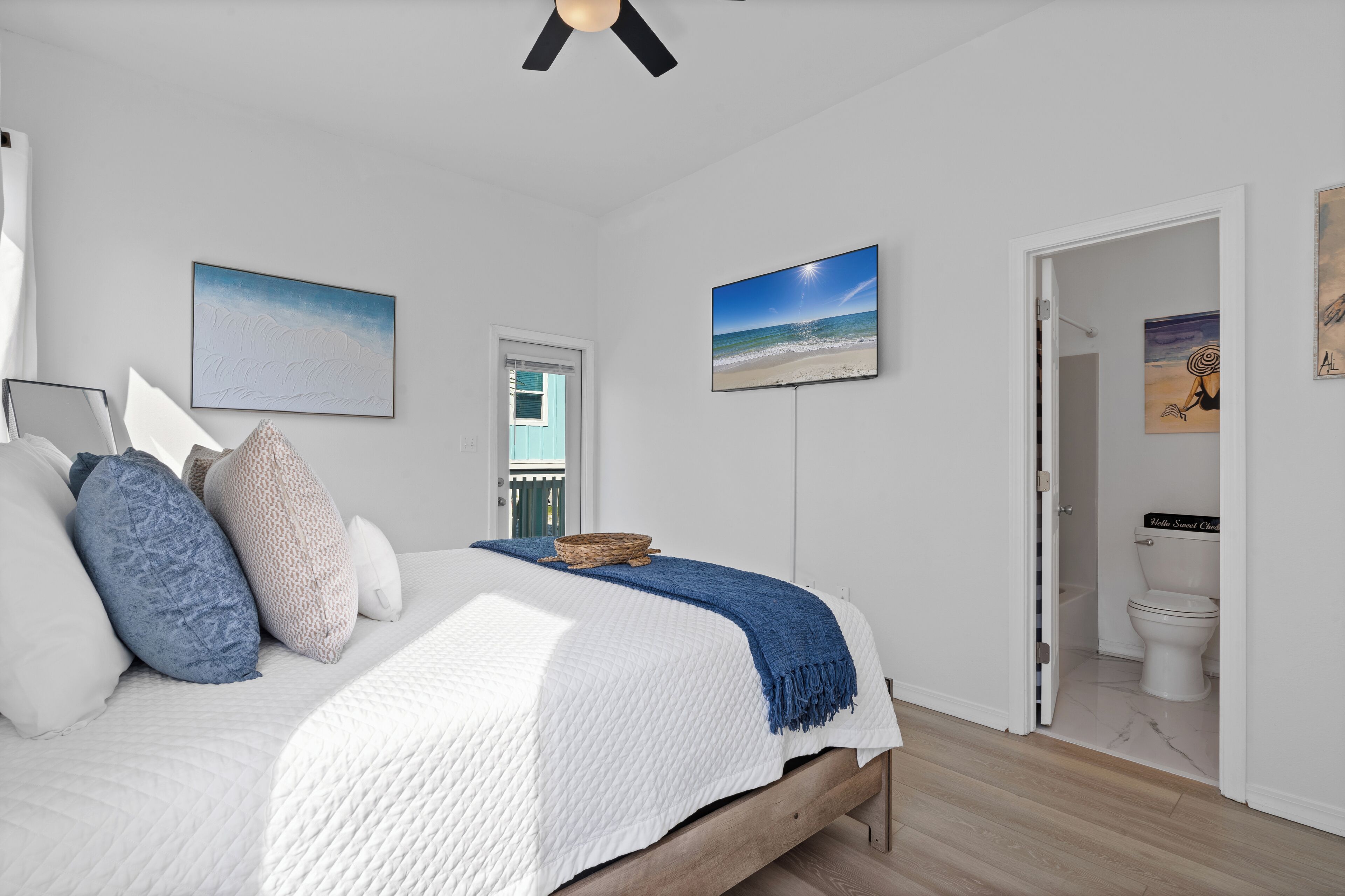 Une chambre à coucher avec un lit, des oreillers, un ventilateur de plafond et des œuvres d’art accrochées aux murs.