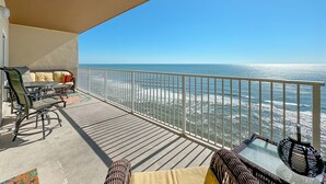 A balcony with a view of the ocean, furnished with a table and chairs, and a glass-top table with a decorative item. - Crystal Shores West 1003 | Indoor/Outdoor Pools, Fitness, Sauna & more | My Beach Getaways (Gulf Shores)