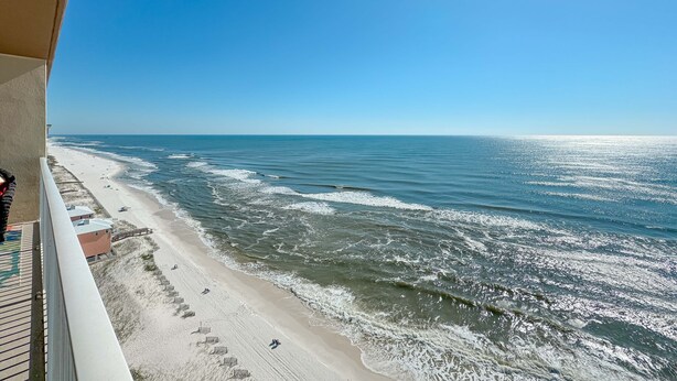 A beach view from a balcony with a clear sky, sandy beach, and ocean waves. - Crystal Shores West 1003 | Indoor/Outdoor Pools, Fitness, Sauna & more | My Beach Getaways (Gulf Shores)