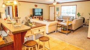 A spacious living area with a kitchen counter, bar stools, a sofa, and a television. - Charming 3-bedroom house on the water with a dock, close to Belhaven & Bath NC. (Belhaven)