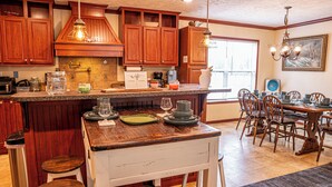 A kitchen with wooden cabinets, a granite countertop, and a dining area with wooden chairs and a table. - Charming 3-bedroom house on the water with a dock, close to Belhaven & Bath NC. (Belhaven)