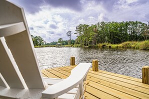 A wooden dock with a white chair facing a calm lake, surrounded by trees and a gazebo in the distance. - Charming 3-bedroom house on the water with a dock, close to Belhaven & Bath NC. (Belhaven)