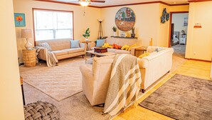 A living room with a sofa, armchairs, a coffee table, and a ceiling fan. There is a window with blinds, a lamp, and a decorative painting on the wall. - Charming 3-bedroom house on the water with a dock, close to Belhaven & Bath NC. (Belhaven)