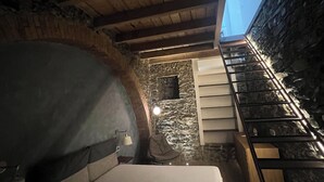 A cozy room with a bed, a chair, a small table, and a stone wall.