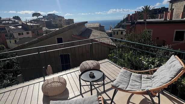 A rooftop terrace with wicker lounge chairs, a small round table, and a potted plant.