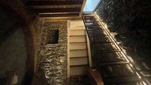 A rustic interior with a wooden ceiling, stone walls, and a staircase leading to an upper level.